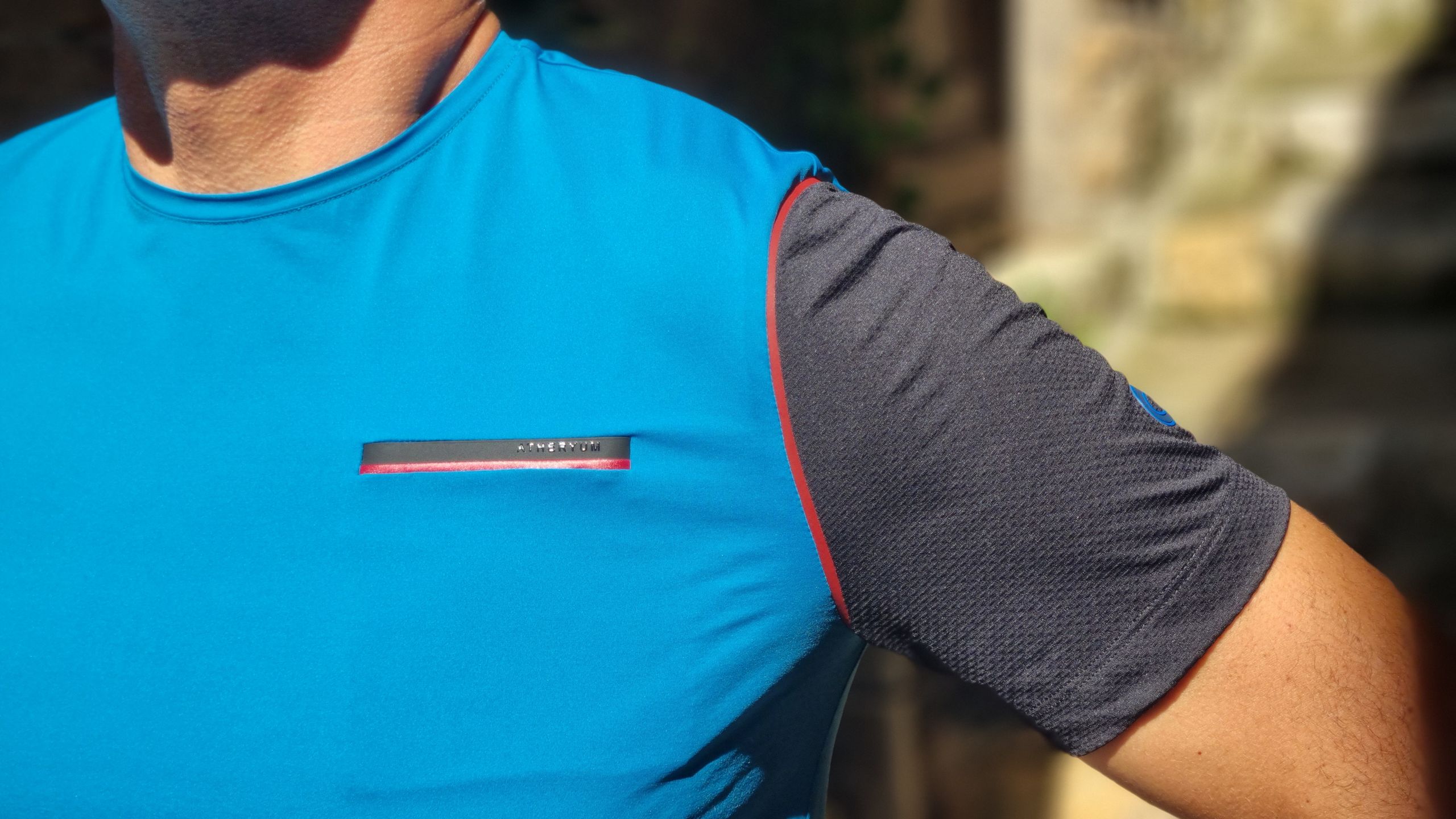 Uomo indossa t-shirt tecnica Atheryum blu con taschino bonded sul petto e manica a contrasto nera e dettaglio logo in TPU